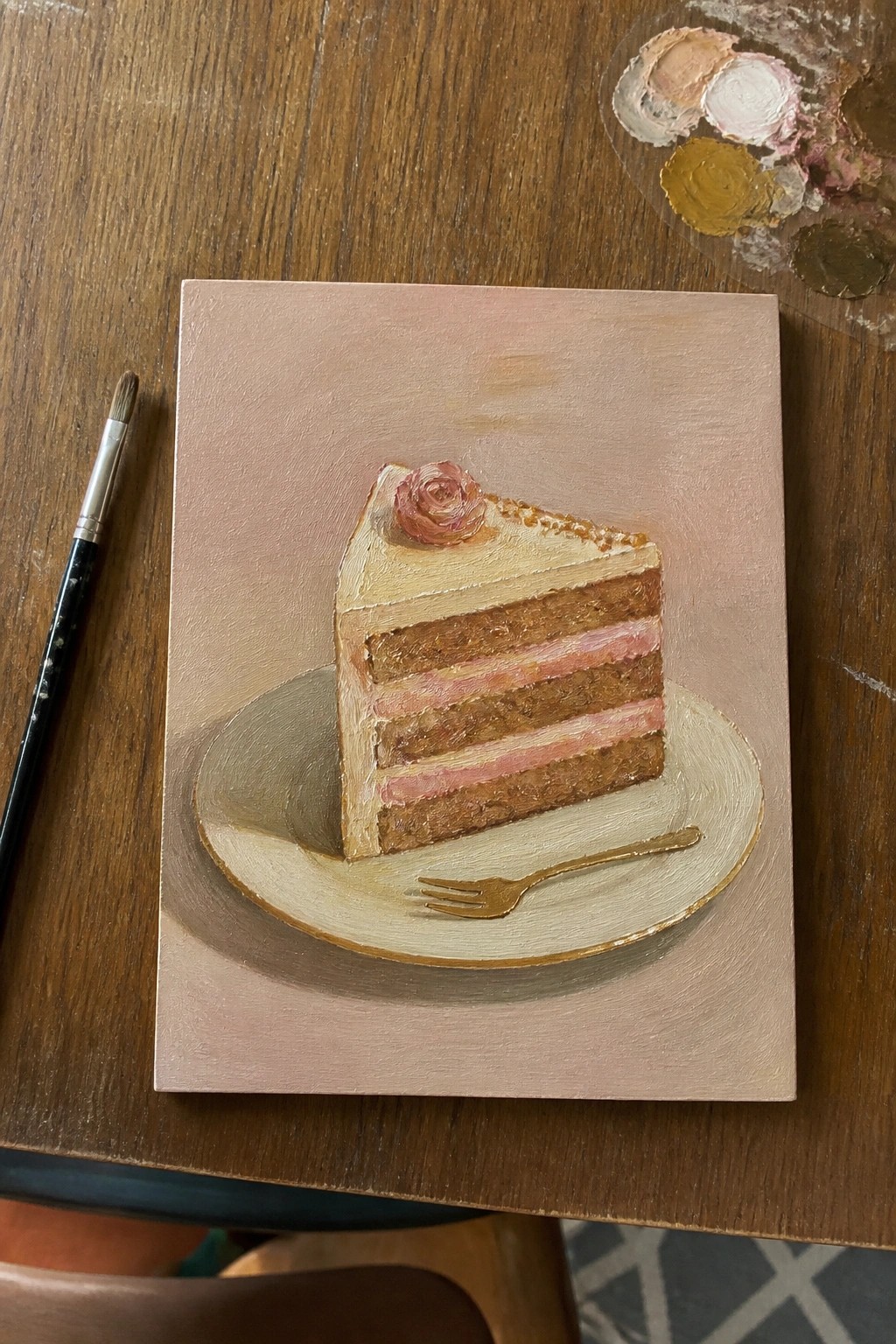 Oil painting of layered cake slice on plate with fork, brush and palette nearby