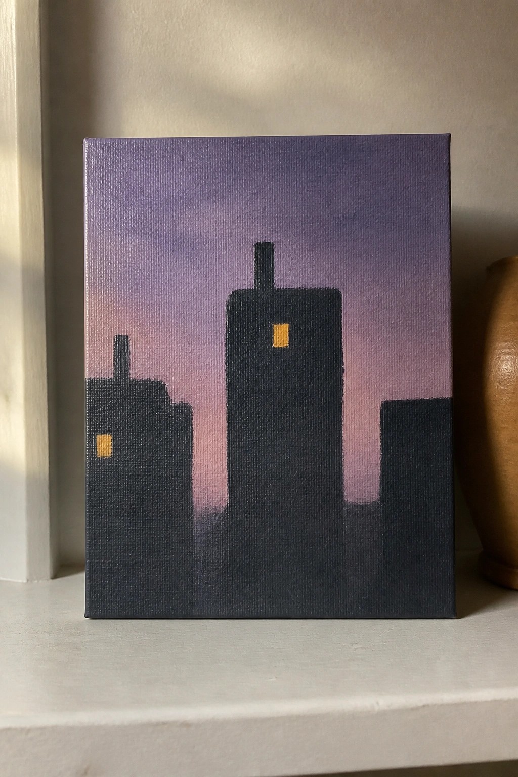 Silhouetted city buildings in dark tones with yellow windows against a purple gradient sky