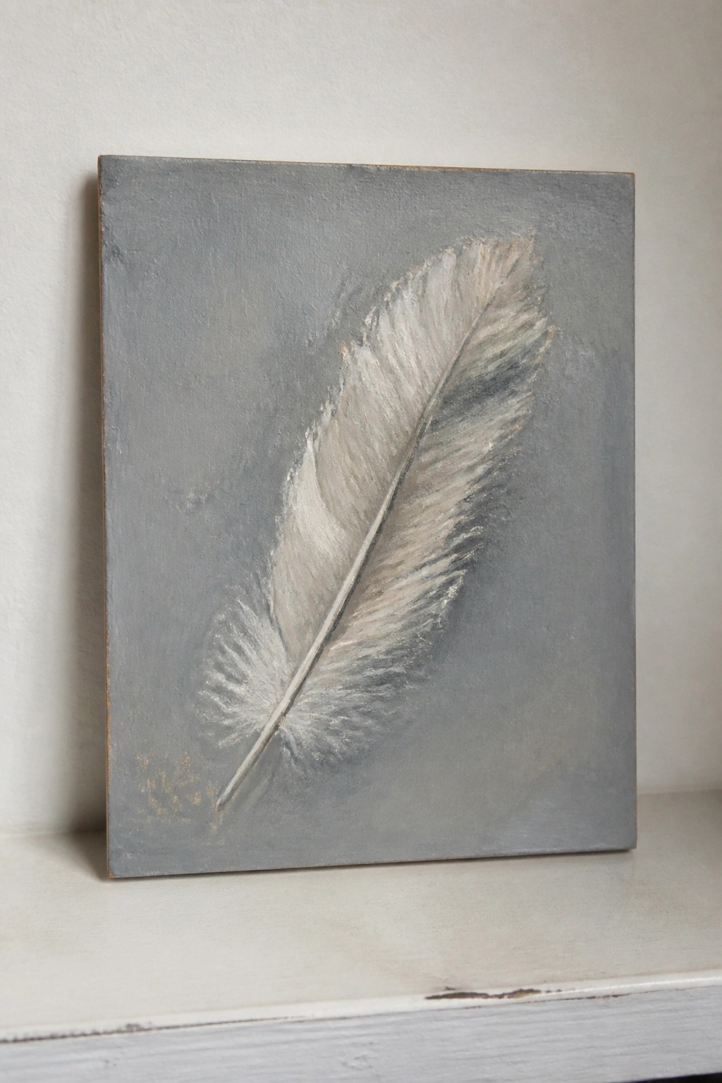 Gray canvas with white-gray feather painting on white ledge against wall