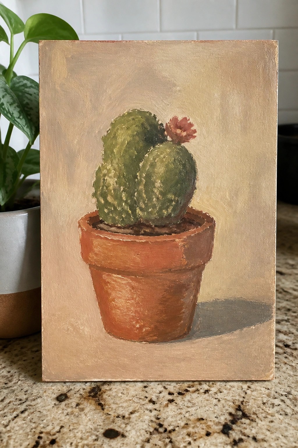 Painting of cactus with red flower in terracotta pot on granite counter