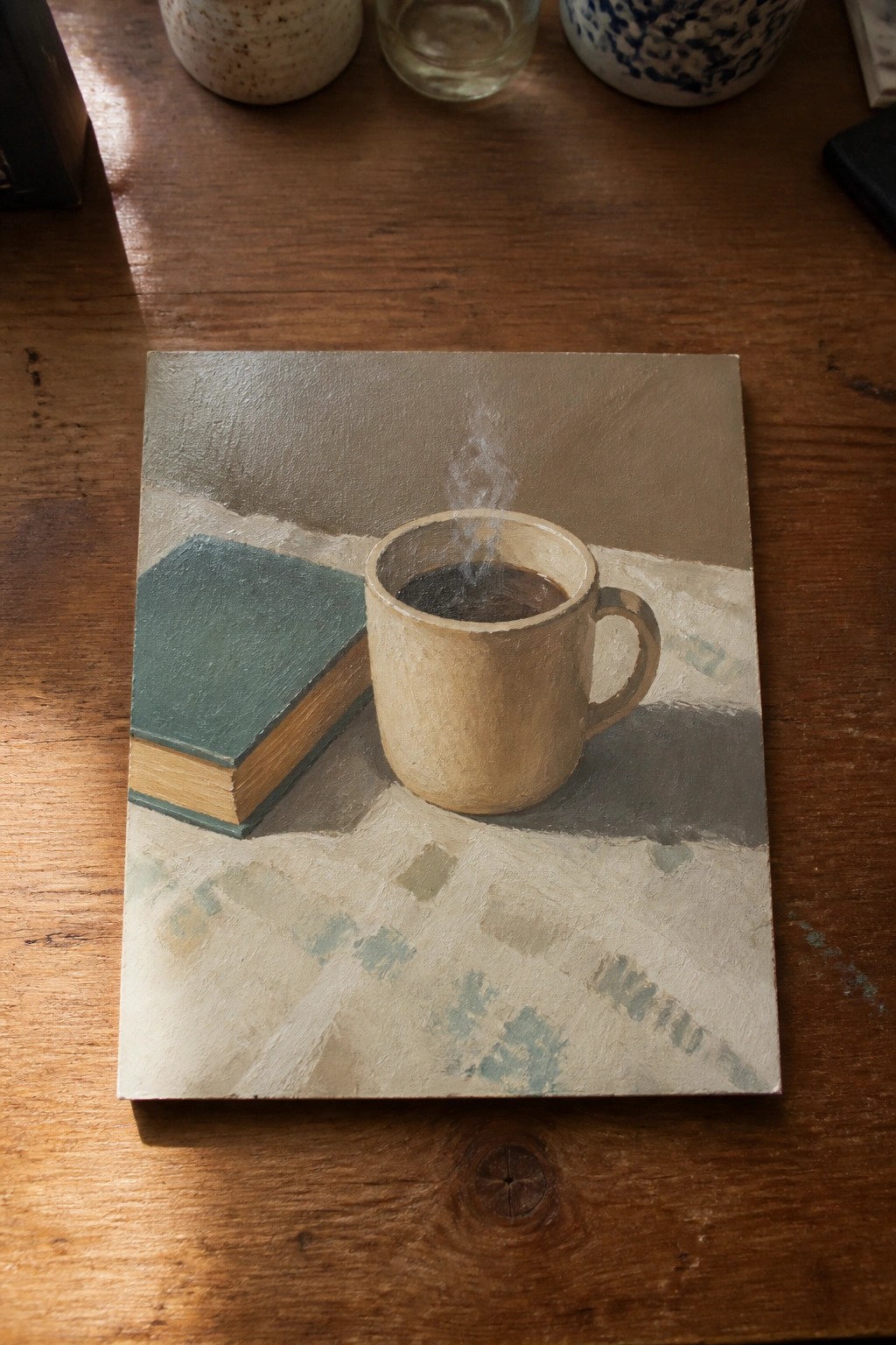 Realistic painting of steaming beige coffee mug beside green book on wood