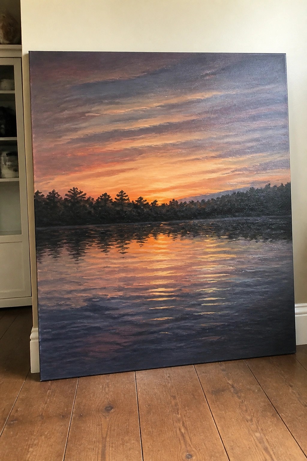 Large landscape painting of vibrant sunset over lake with tree silhouettes on floor