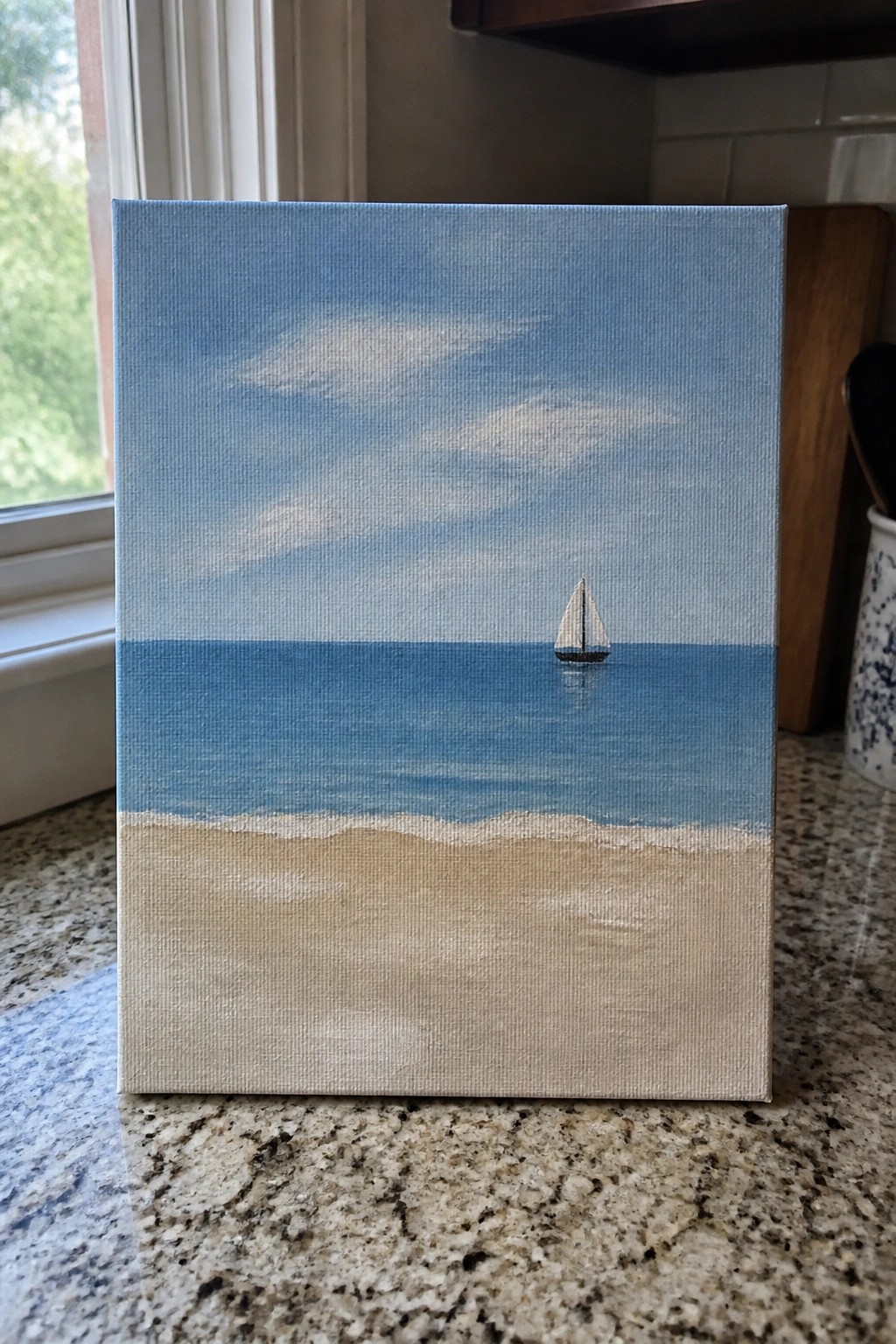 Canvas painting of sailboat on blue ocean above sandy beach on granite counter