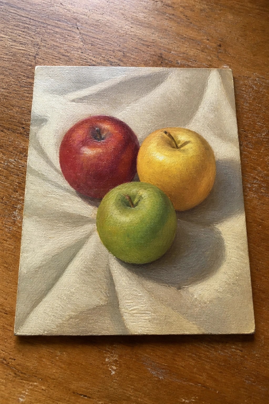 Three red, yellow, and green apples on draped white cloth over wood.