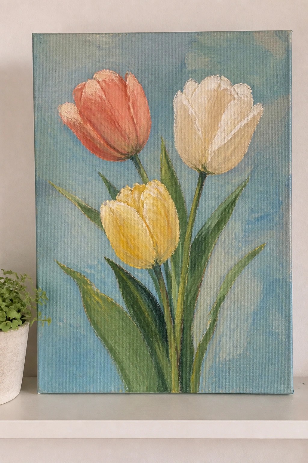 Painting of coral, white, and yellow tulips with green leaves on blue canvas background