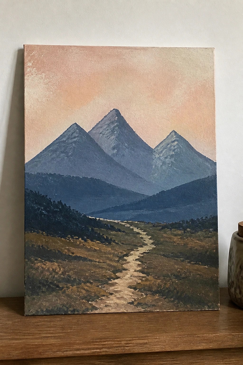 Landscape painting of three blue mountains with winding path through grassy valley at dusk