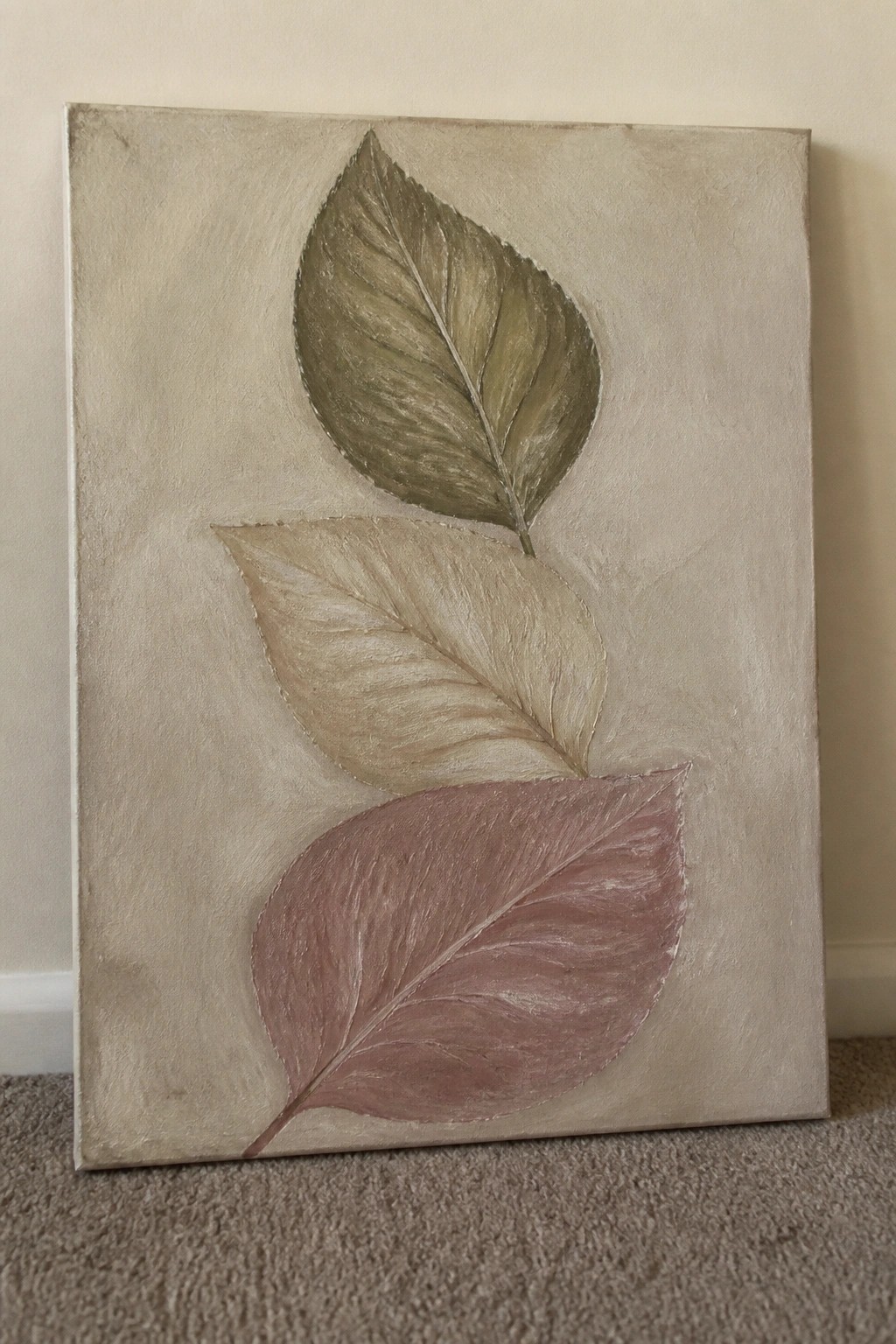 Three overlapping leaves in green, beige, and pink on textured canvas