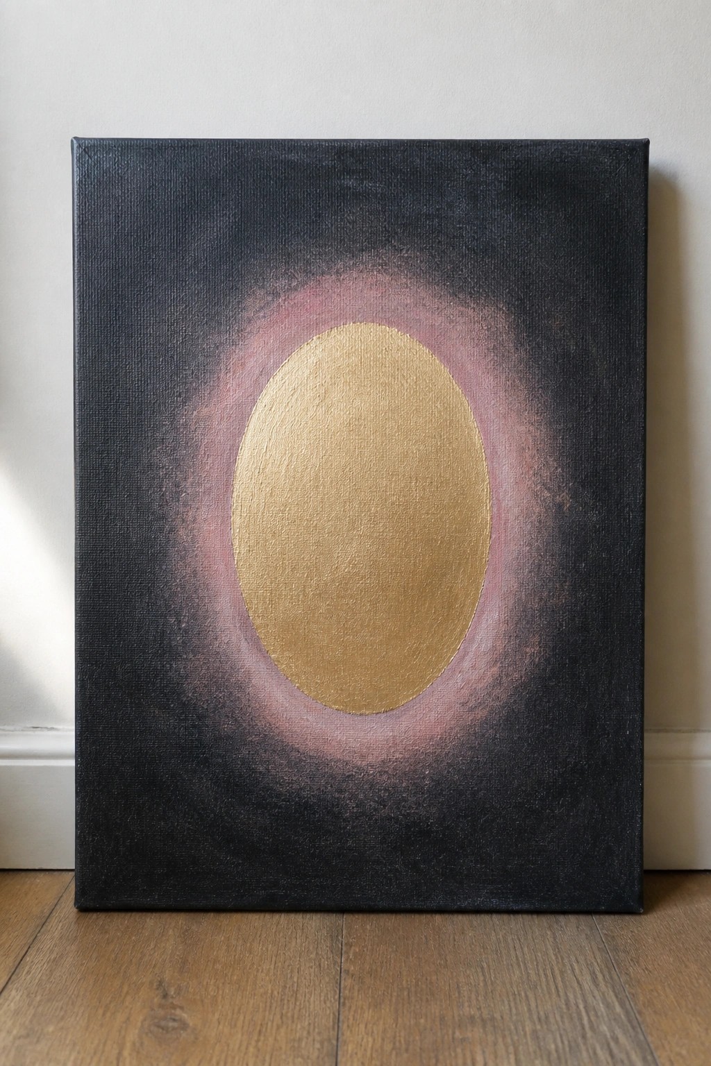 Abstract canvas with central gold oval, pink halo on black background, leaning on floor