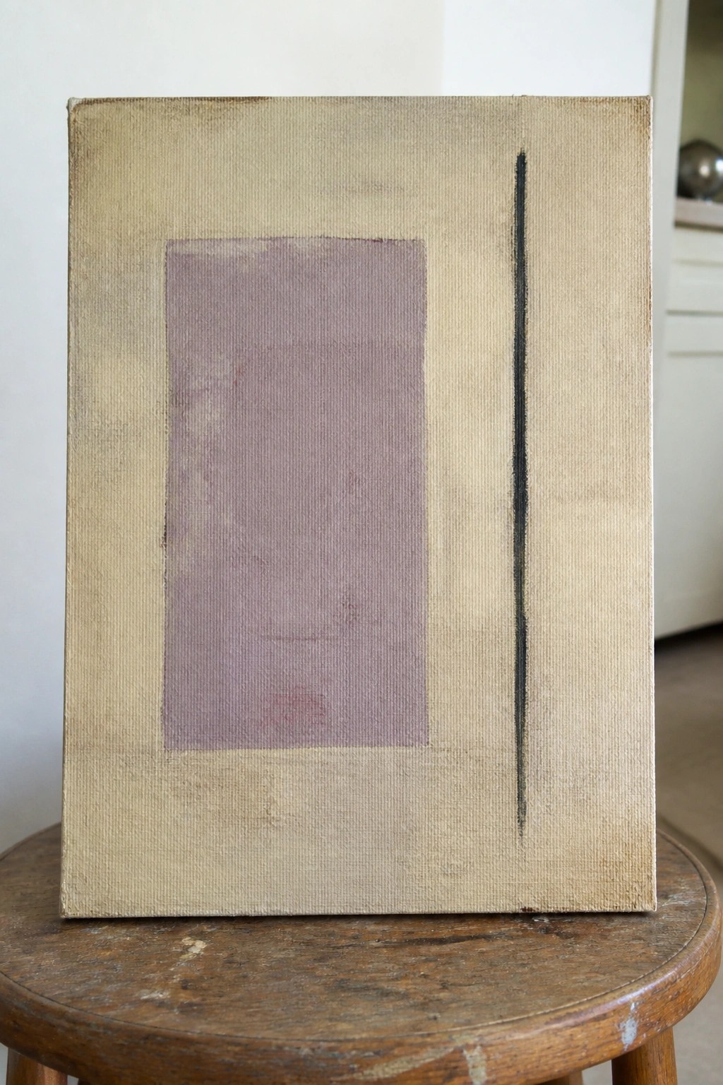 Abstract canvas with muted purple rectangle and thin black line on wooden stool