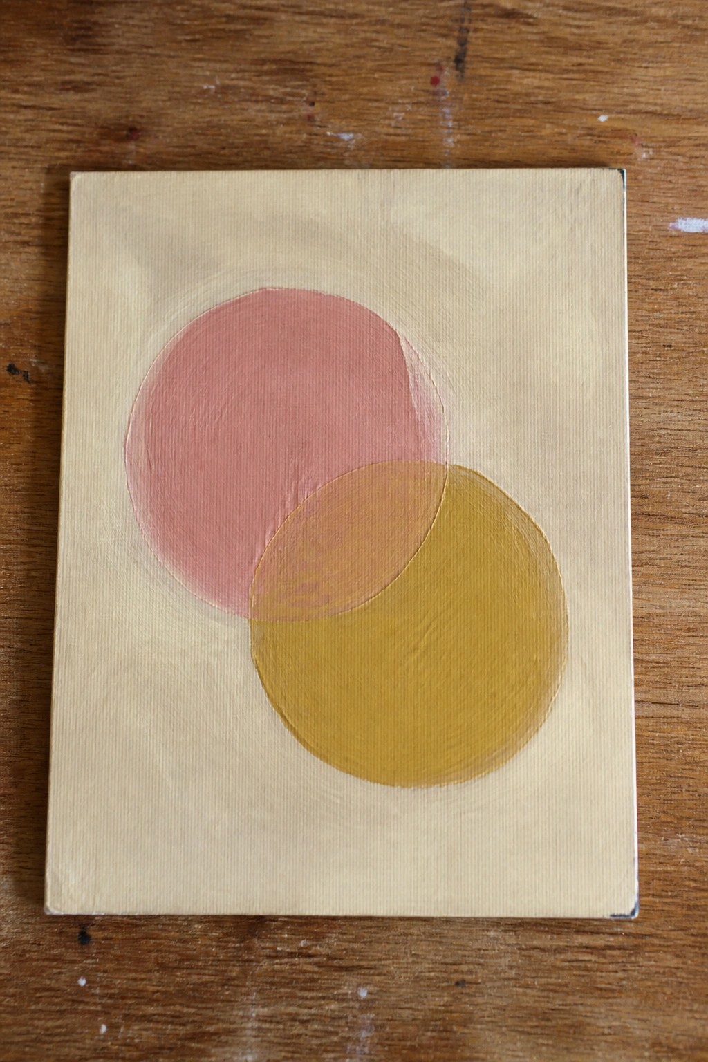 Abstract painting of overlapping pink and yellow circles on beige canvas atop wood.