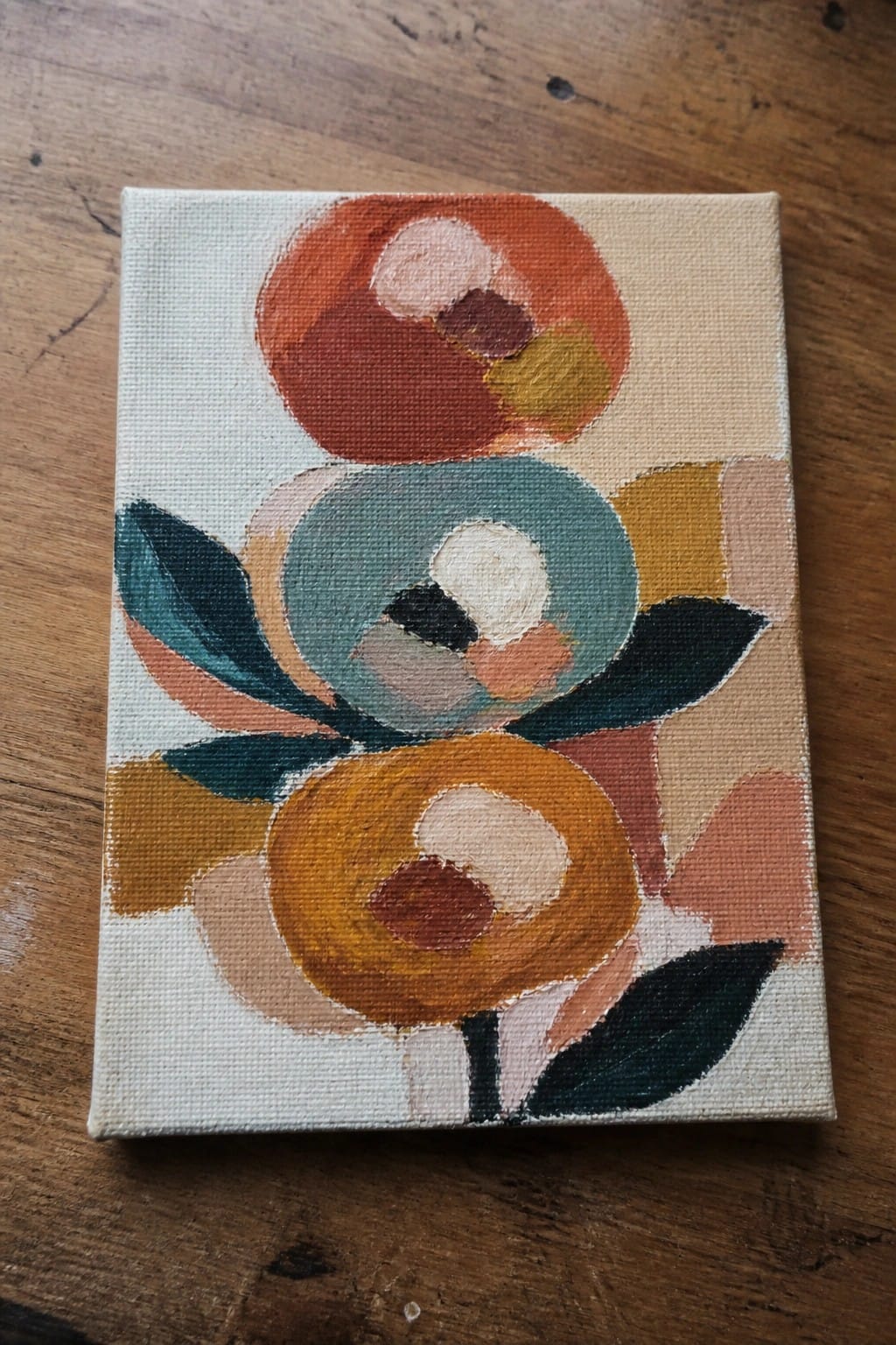 Abstract canvas painting of colorful overlapping circles forming flowers on wood table.