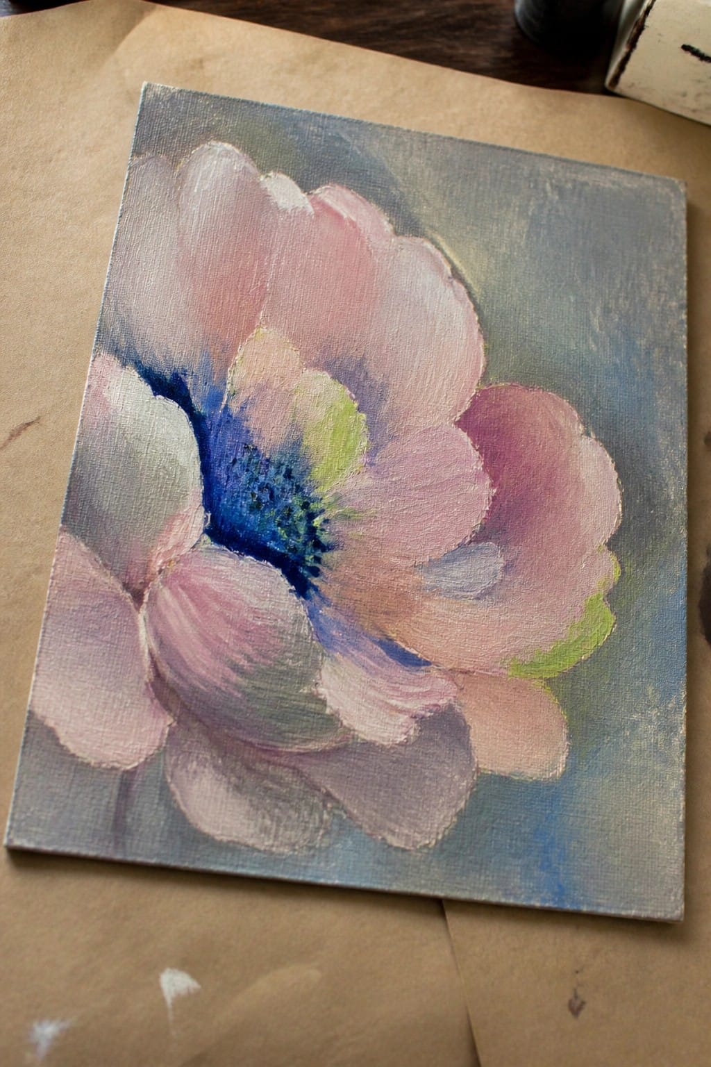 Impressionistic painting of a pink flower with blue-green center on canvas