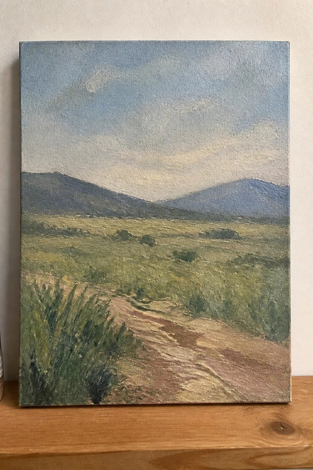 Oil painting of dirt path through green fields toward hazy blue mountains under cloudy sky