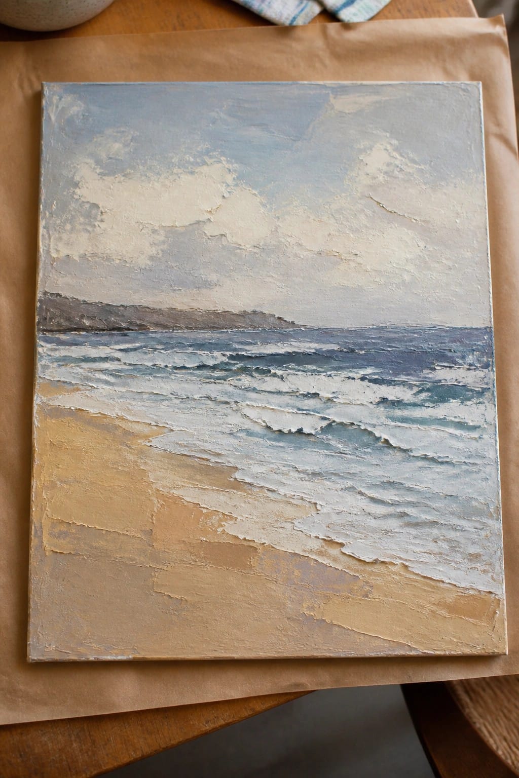 Thickly textured seascape painting of waves and sandy beach on brown paper over wood