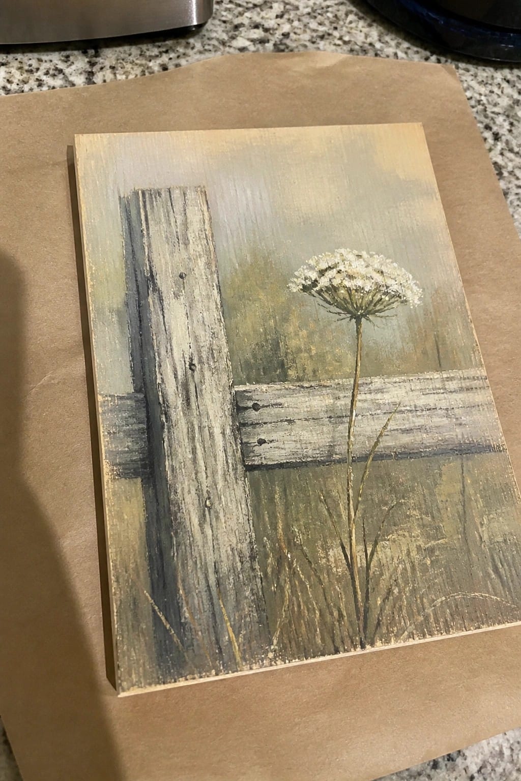 Weathered wooden fence with white wildflower against muted green-gray landscape on painted board