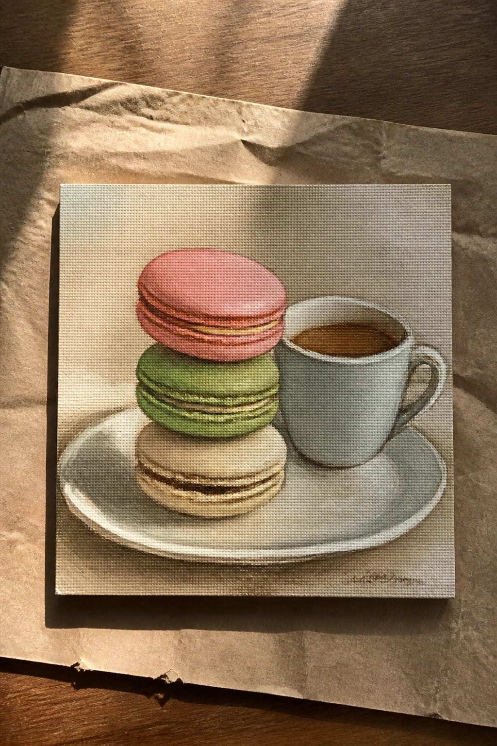 Still life painting of stacked pink, green, and beige macarons beside coffee cup.