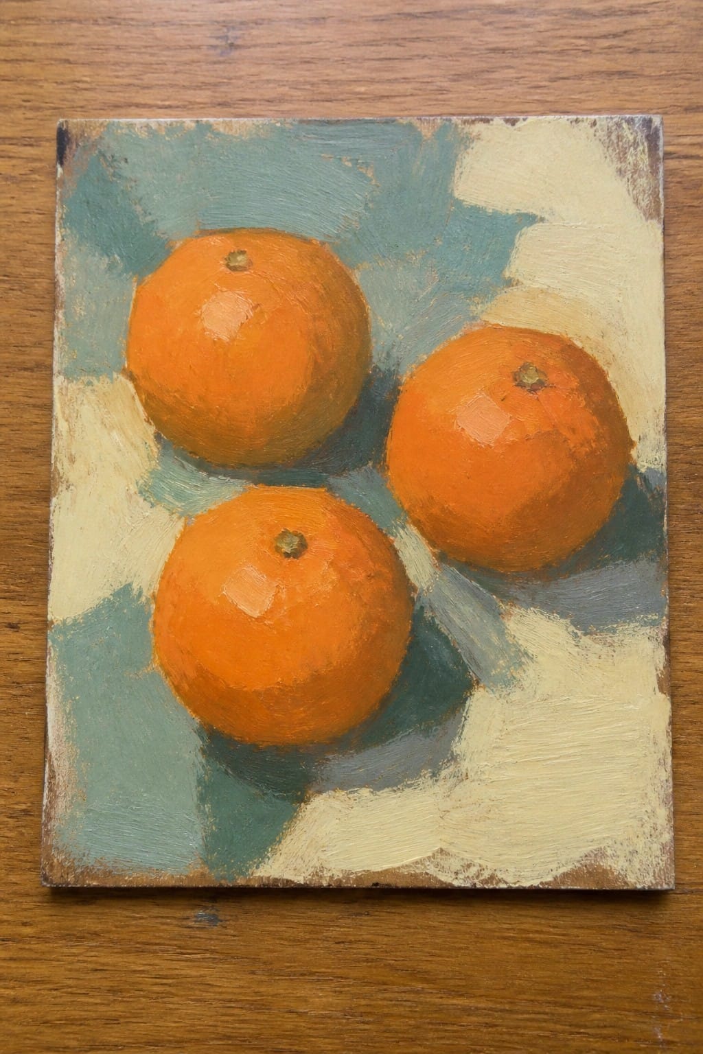 Three oranges in an oil painting with teal and cream background on wood