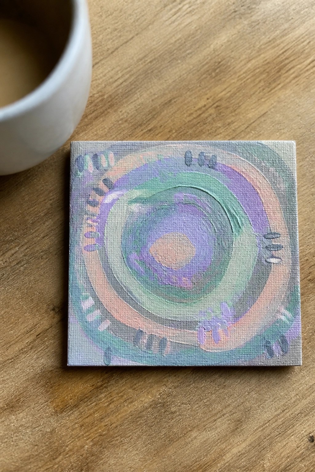 Abstract pastel painting of concentric circles on wood beside white cup