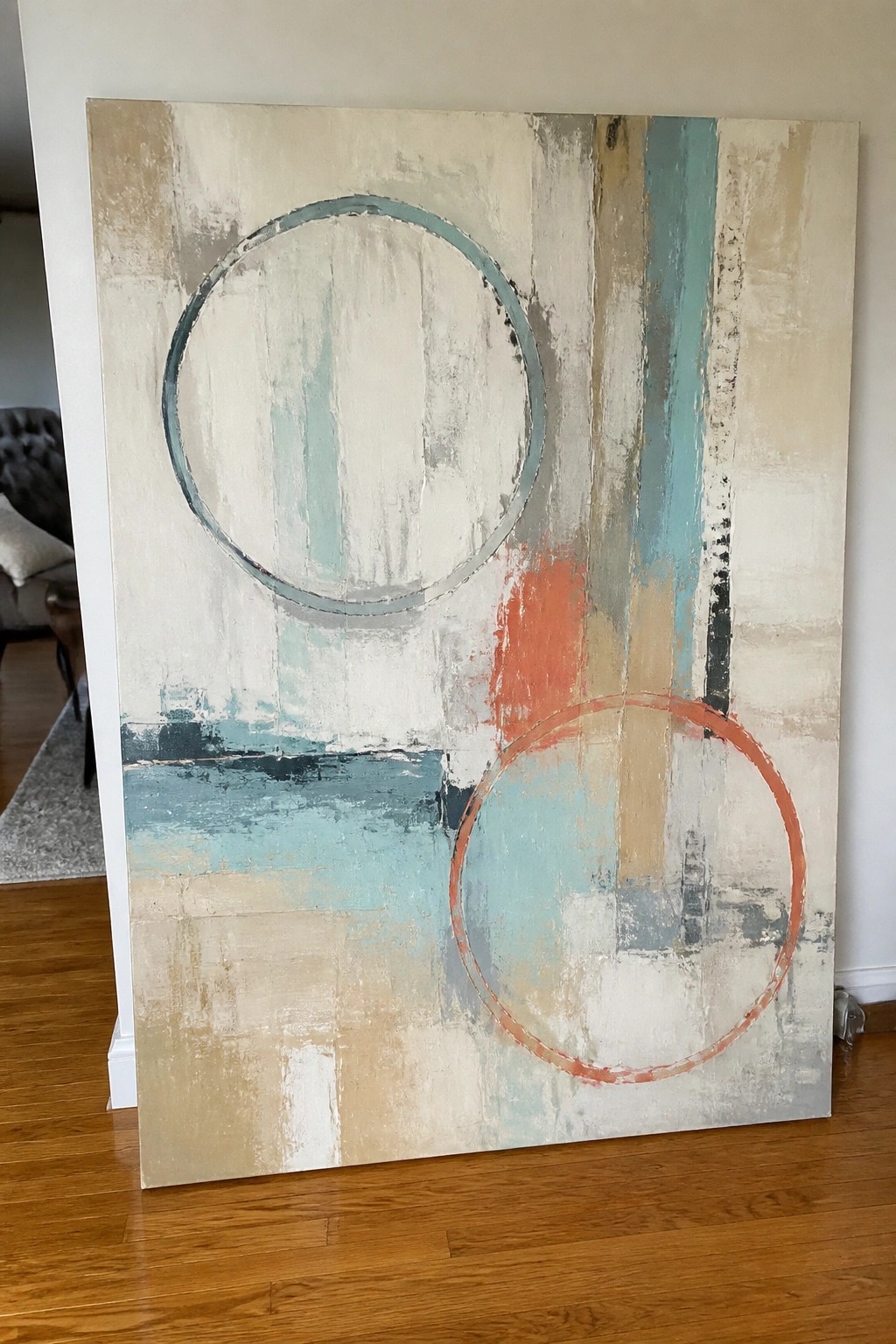 Abstract painting with teal and orange circles on beige canvas leaning against wall.