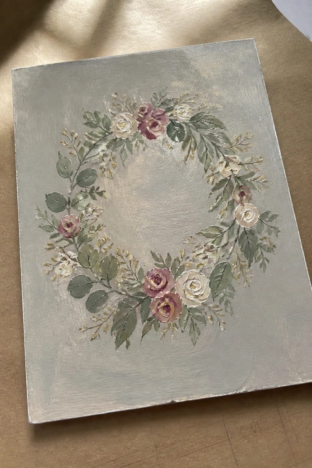 Floral wreath with pink and white roses, green leaves on gray canvas.