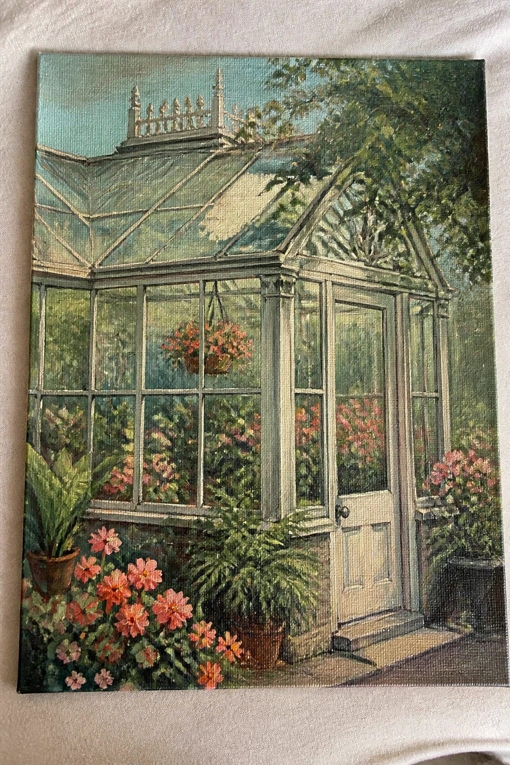 White-framed glass greenhouse with open door, hanging flowers, and lush pink blooms.