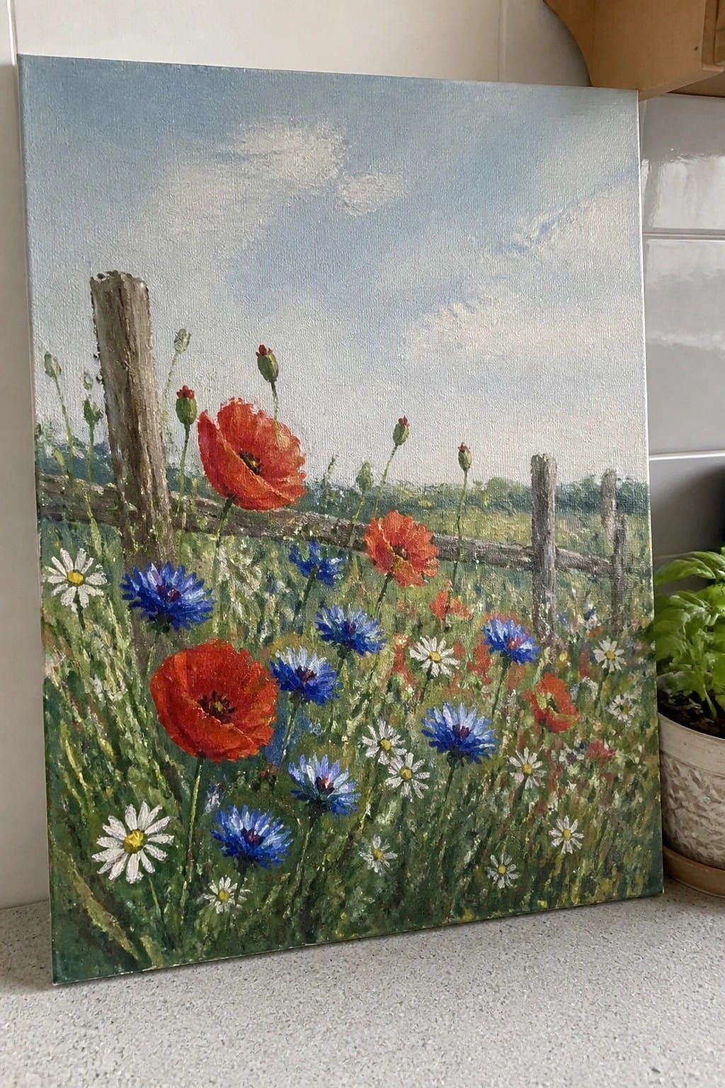 Vibrant wildflower meadow painting with red poppies, blue cornflowers, white daisies, and fence.