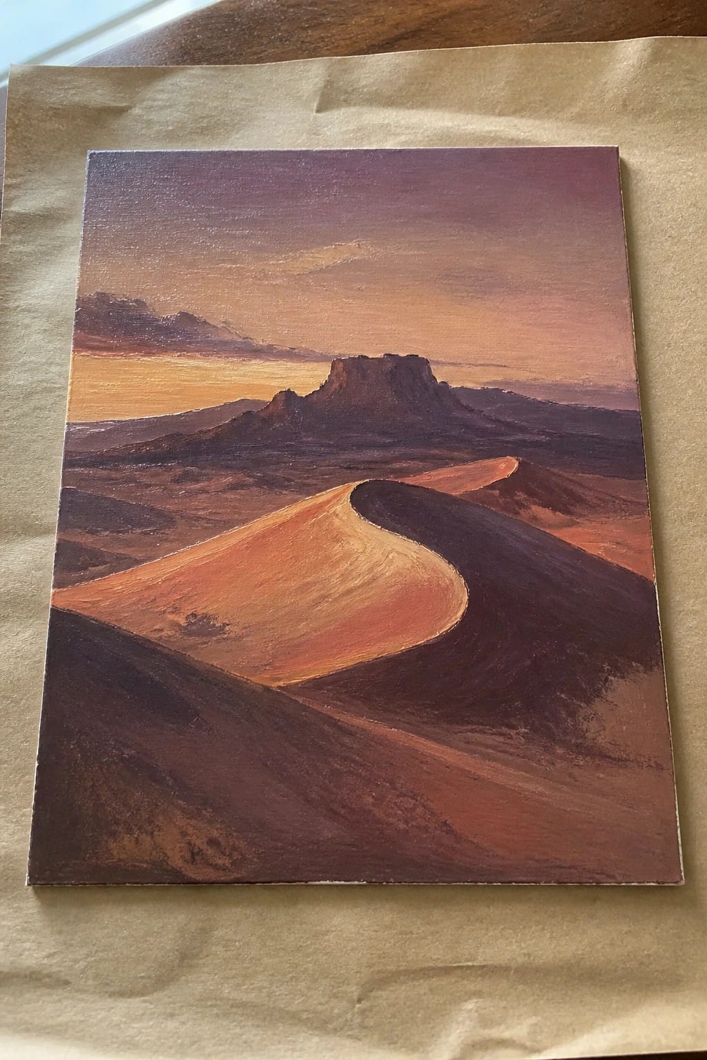 An oil painting of a desert landscape at sunset with a prominent mesa in the background and rolling orange dunes in the foreground.