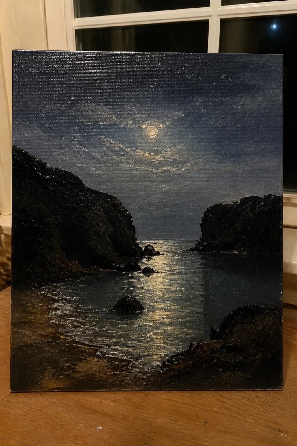 Moonlit seascape painting with dark cliffs, reflective water, and sandy shore at night