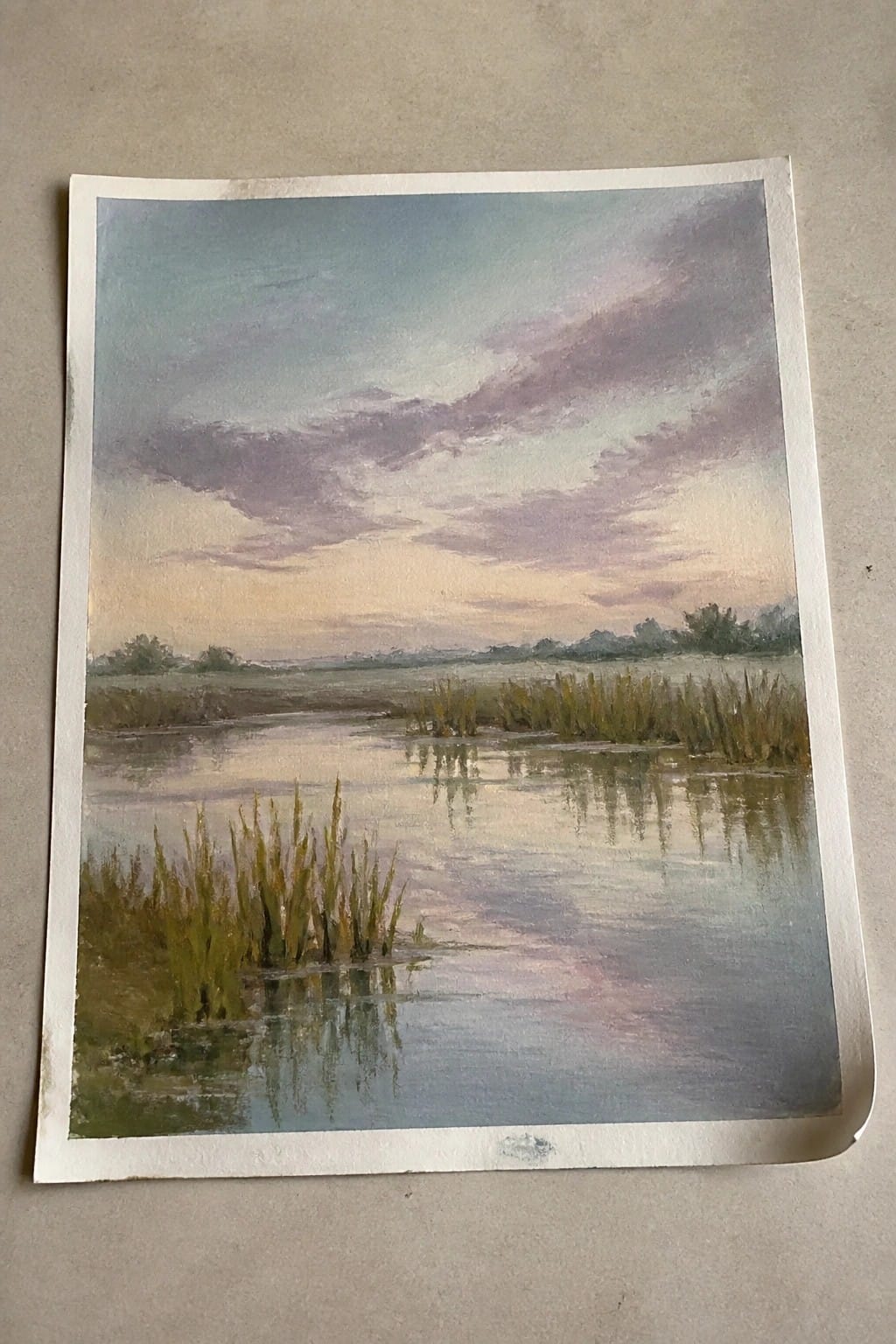 Marsh landscape with reeds reflecting in calm water under a purple-pink sunset sky