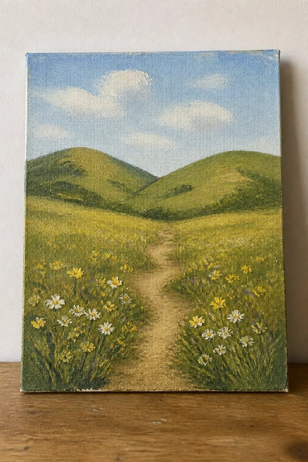 Winding dirt path through meadow of yellow and white wildflowers with green hills beyond.