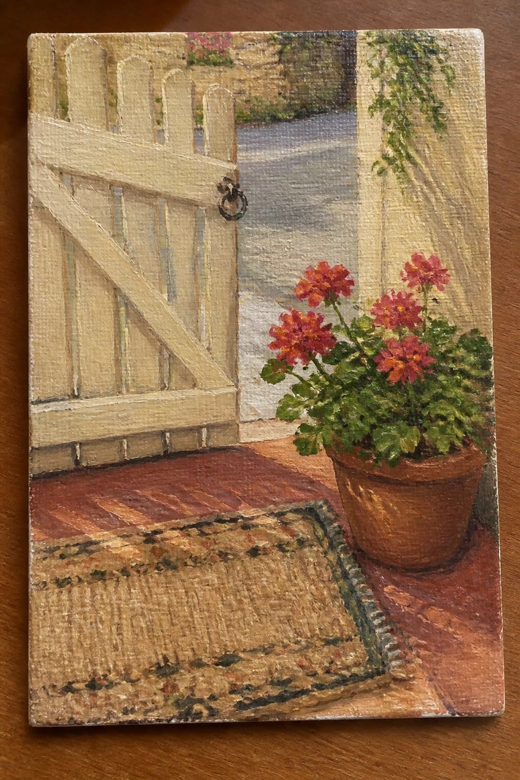 Open wooden gate beside potted red flowers and woven rug on brick floor