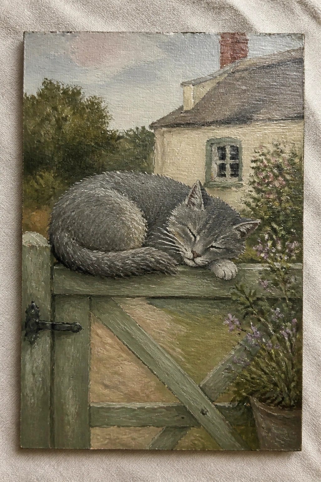 Gray cat sleeping on green wooden gate by cottage with flowers and chimney