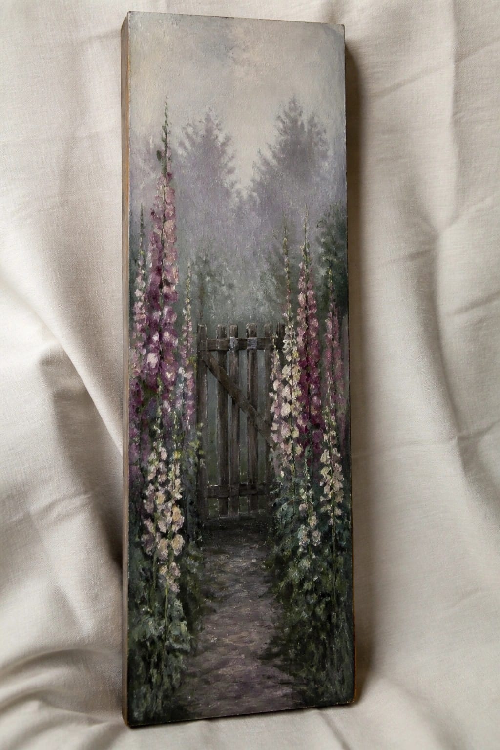 Foggy path through wooden gate lined with tall purple and white hollyhocks