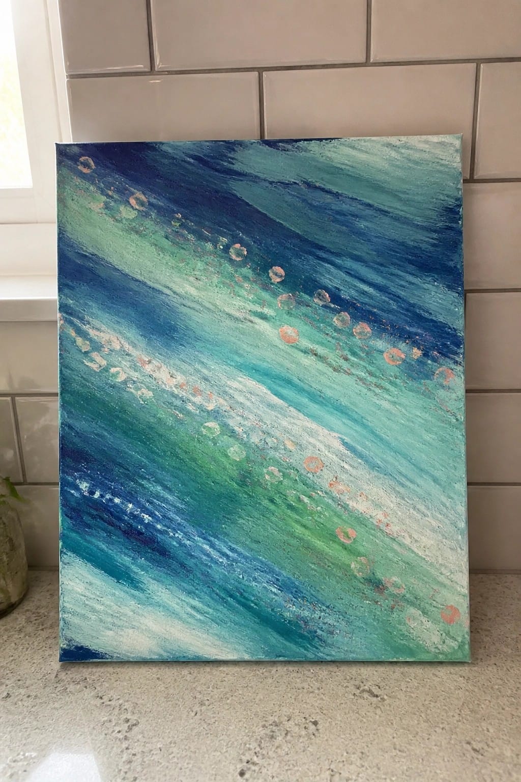 Abstract canvas with swirling blues, greens, and metallic copper circles on countertop