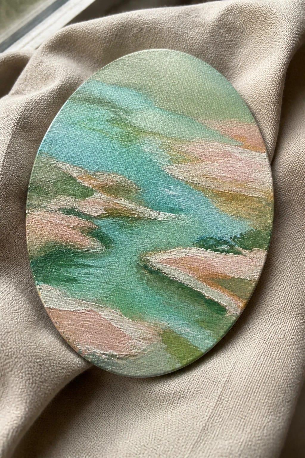 Oval abstract painting with green blue pink brushstrokes on beige fabric