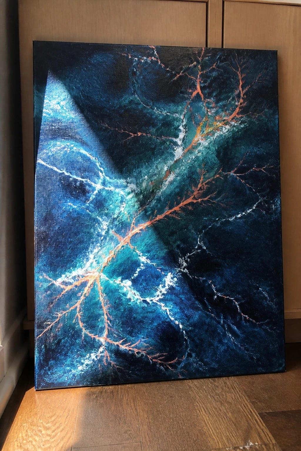 Abstract painting in deep blues and teals with white and orange branching patterns on wooden floor