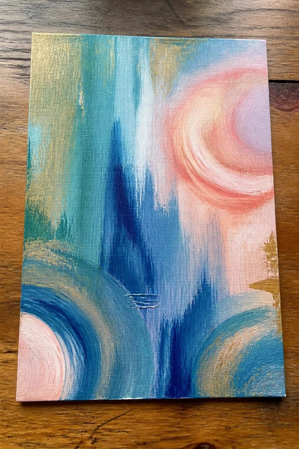 Abstract canvas with swirling blues, pinks, teals, and gold brushstrokes on wood