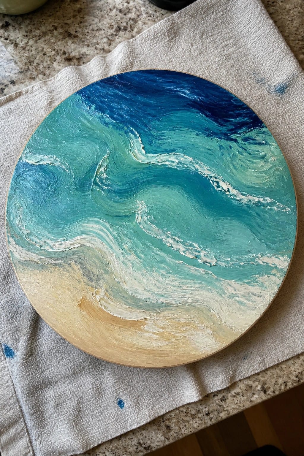 Circular painting of swirling blue ocean waves with white foam on cloth.