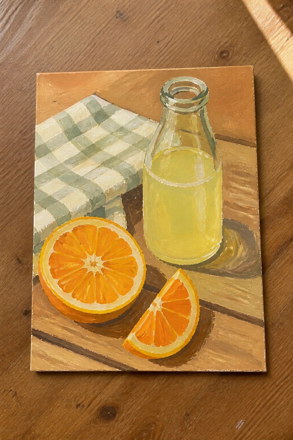 Still life painting of glass bottle with yellow liquid, sliced oranges, and checkered cloth on wood