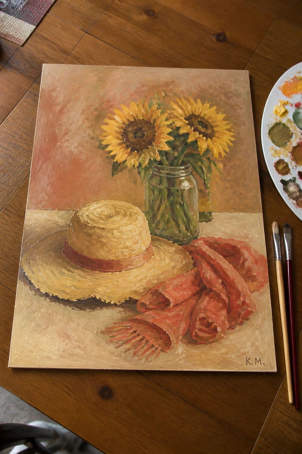 Still life painting of sunflowers in jar, straw hat, red scarf, and paint palette.