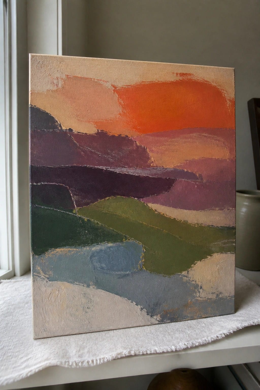 Abstract painting with textured layers of orange, purple, green, and blue on canvas by window.