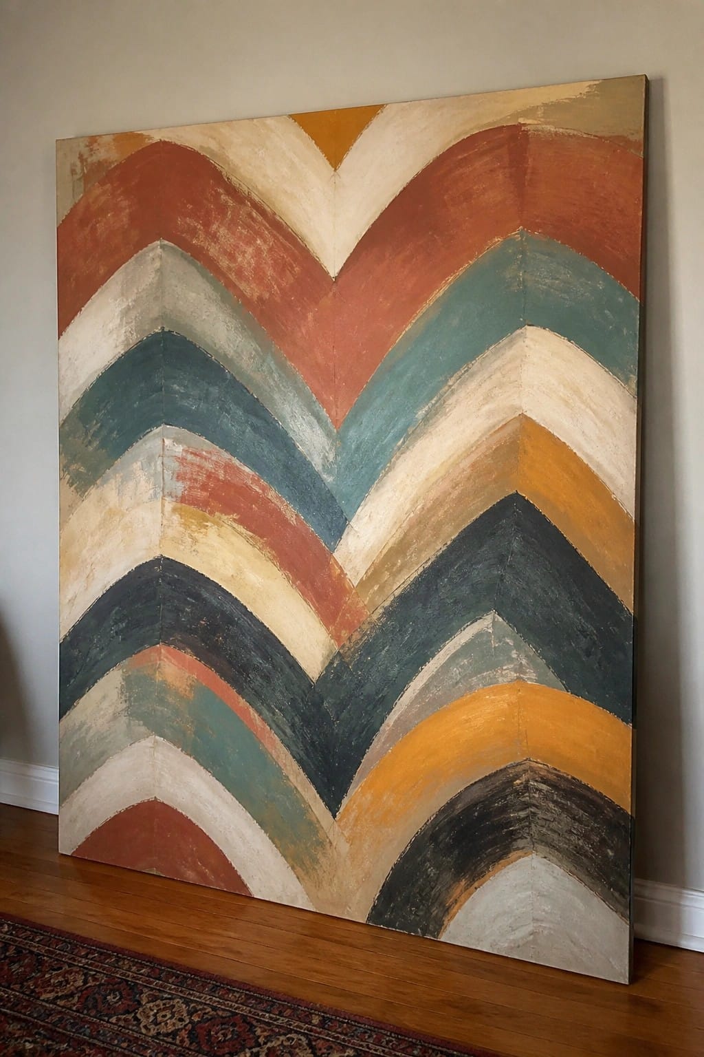 Large abstract chevron painting with earthy tones leaning on wooden floor