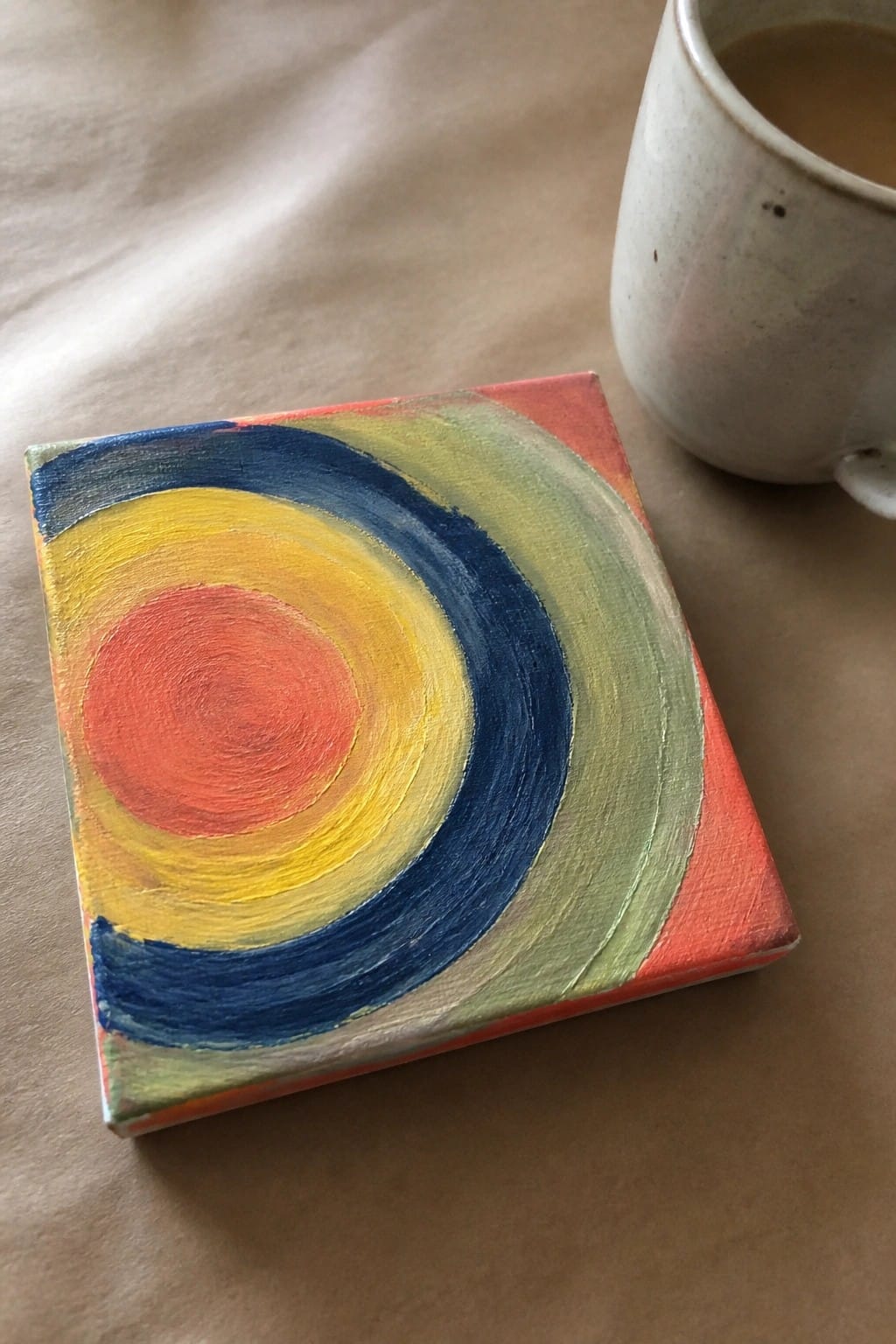 Abstract painting of colorful concentric circles on canvas beside a ceramic mug