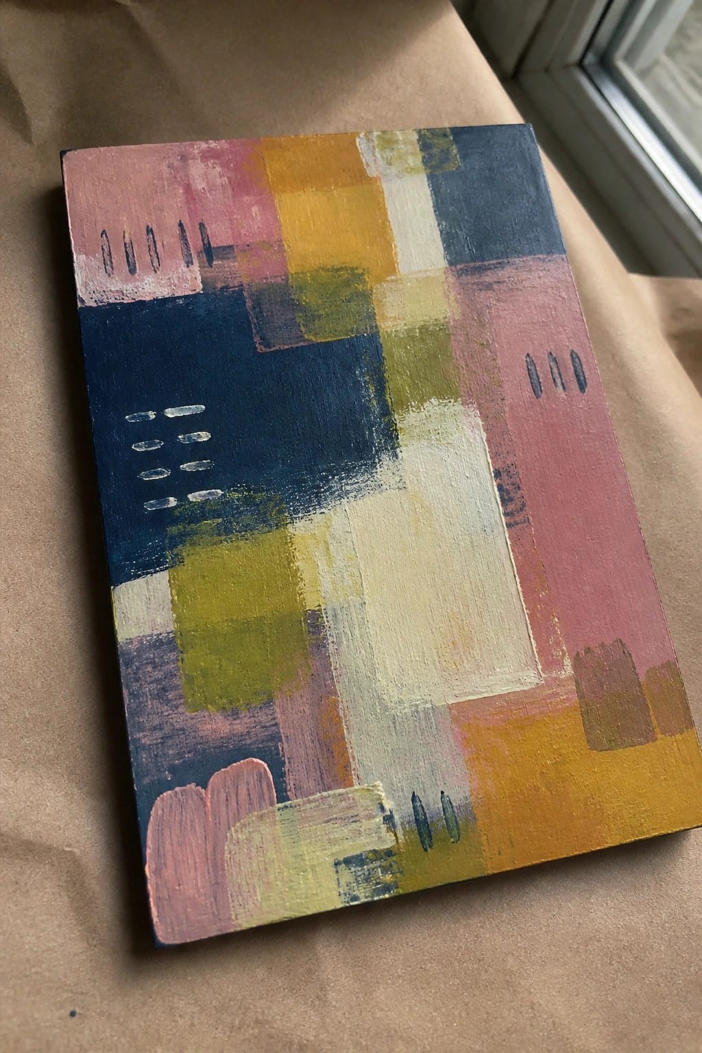 Abstract canvas with pink, blue, yellow geometric blocks and dashed marks on brown paper.