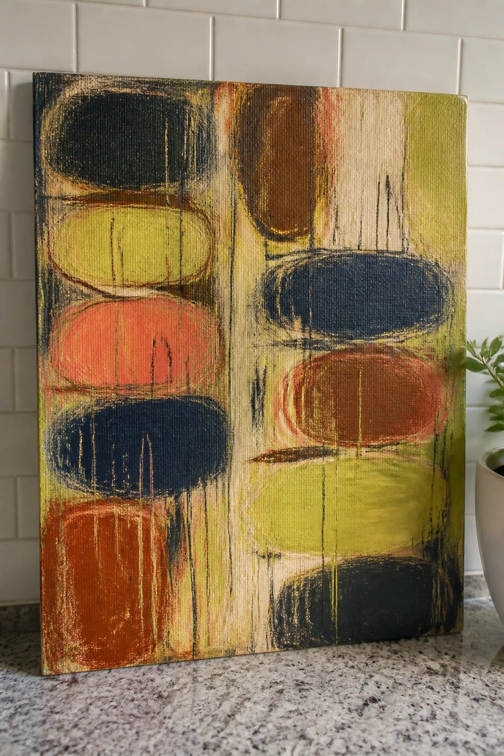 Abstract painting with colorful ovals leaning on granite countertop against white tiles