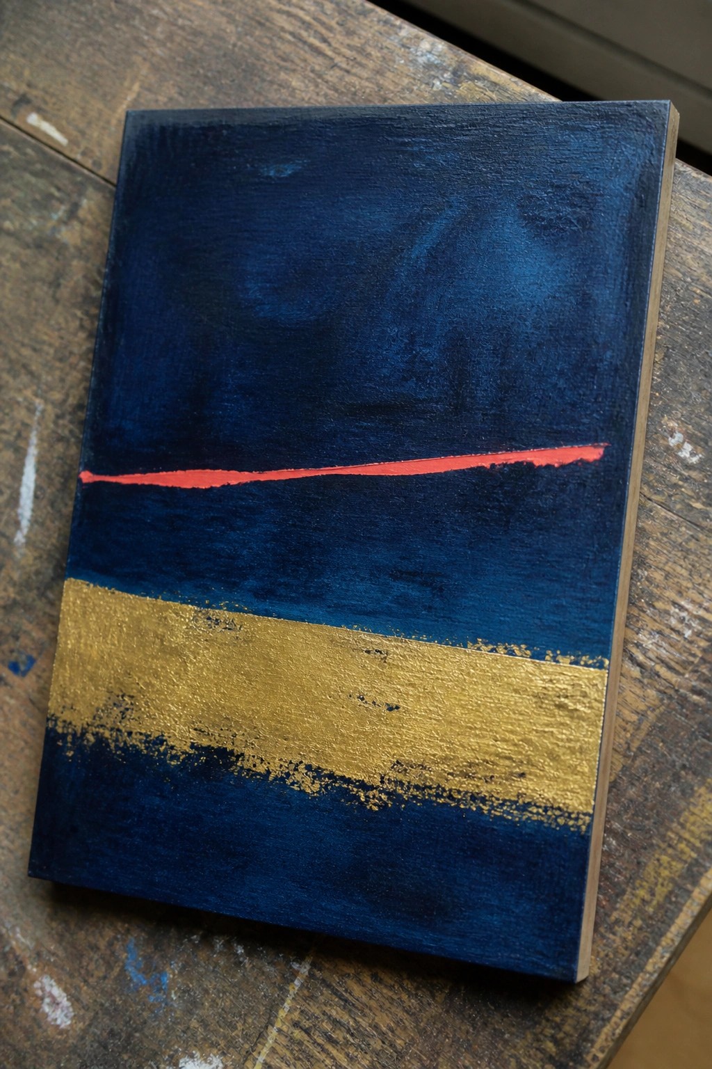 Abstract painting with deep blue sections, thin red line, and wide gold band on wood.