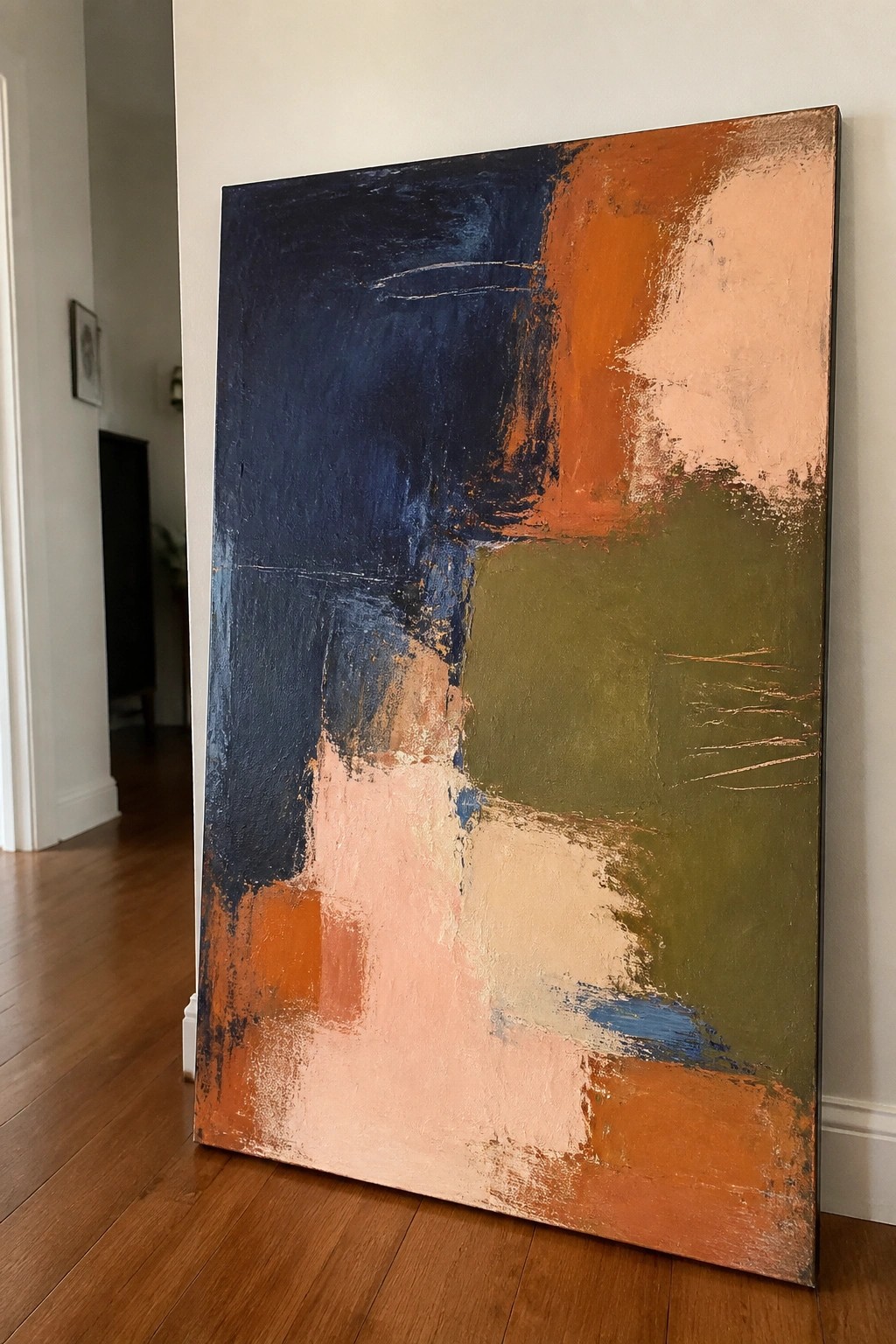Large abstract painting with navy, orange, peach, and olive brushstrokes leaning on wood floor
