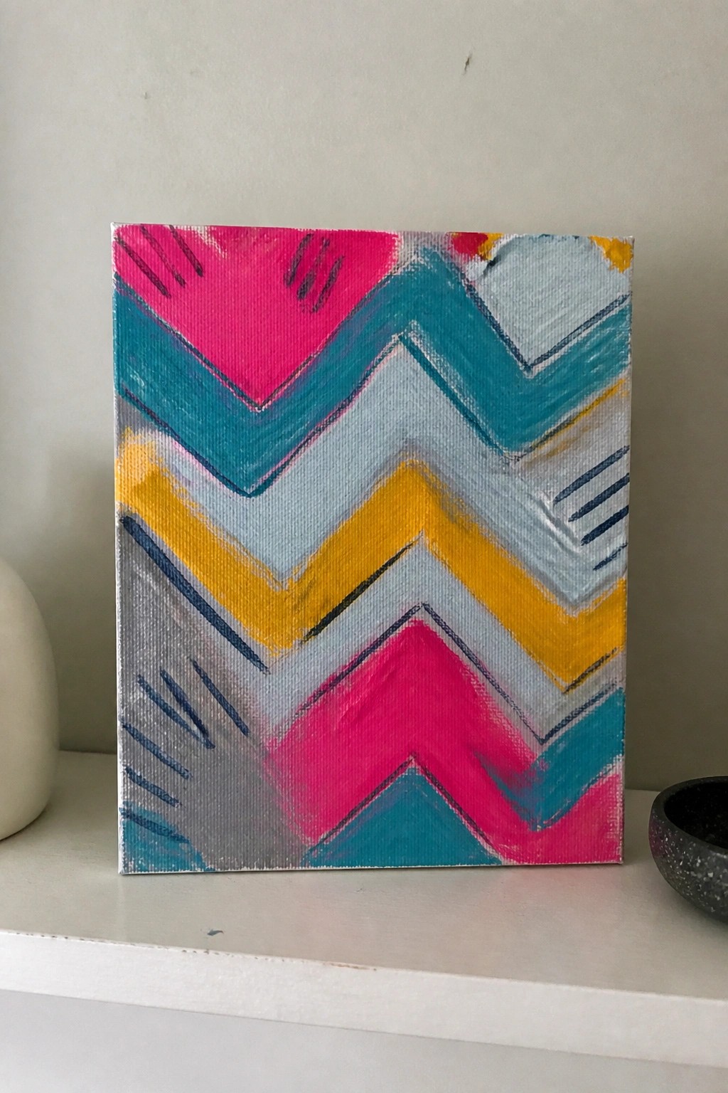 Colorful abstract chevron painting on canvas with pink, teal, yellow, and gray zigzags.