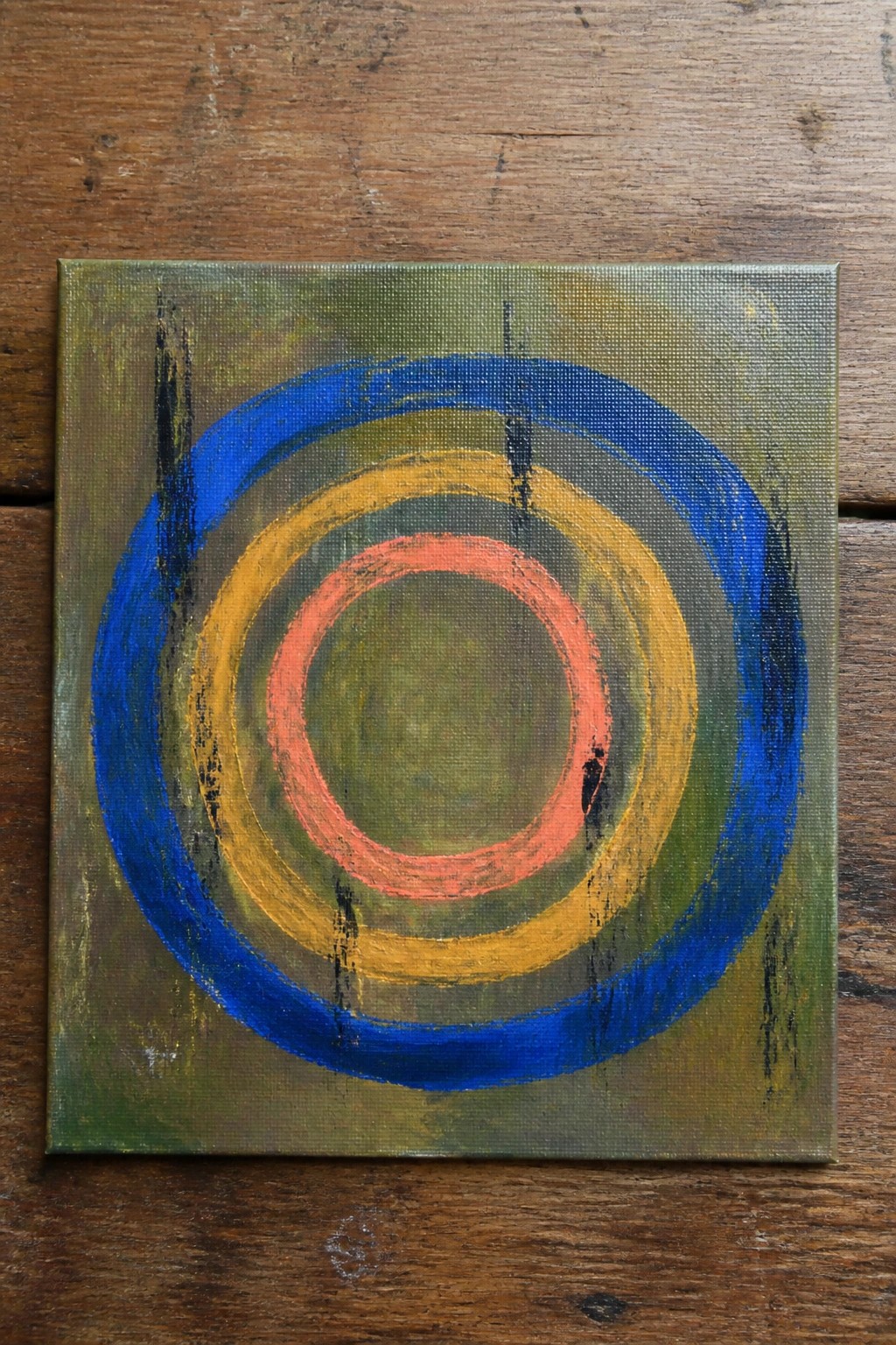 Abstract painting with blue, yellow and coral concentric circles on green canvas.