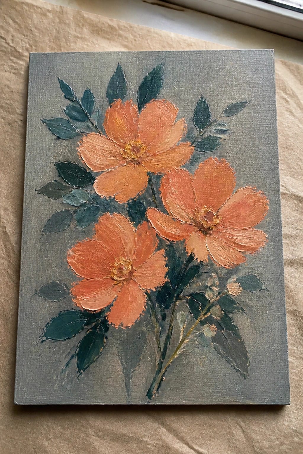 Three orange flowers with green leaves painted in thick strokes on gray canvas.